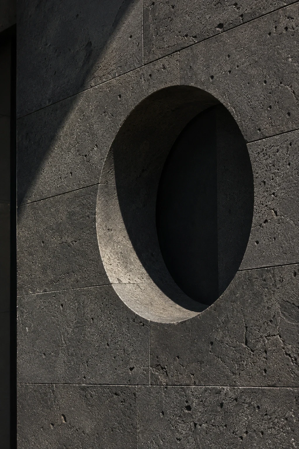Circular opening recessed into a charcoal basalt facade.