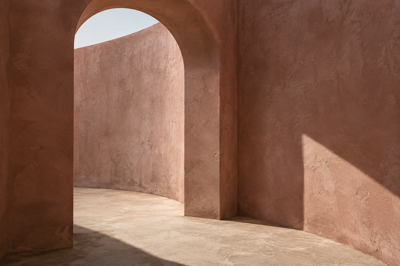 Rose plaster arch and curved courtyard wall in sunlight.